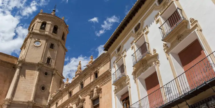 Views of the pinky coloured San Patricio Collegiate Church tower against a blue cloudy sky in the centre of Lorca City in Murcia.